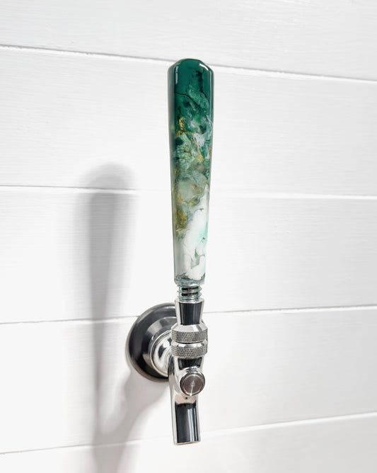 Decorative faucet handle with green marbled design on a white tiled wall.