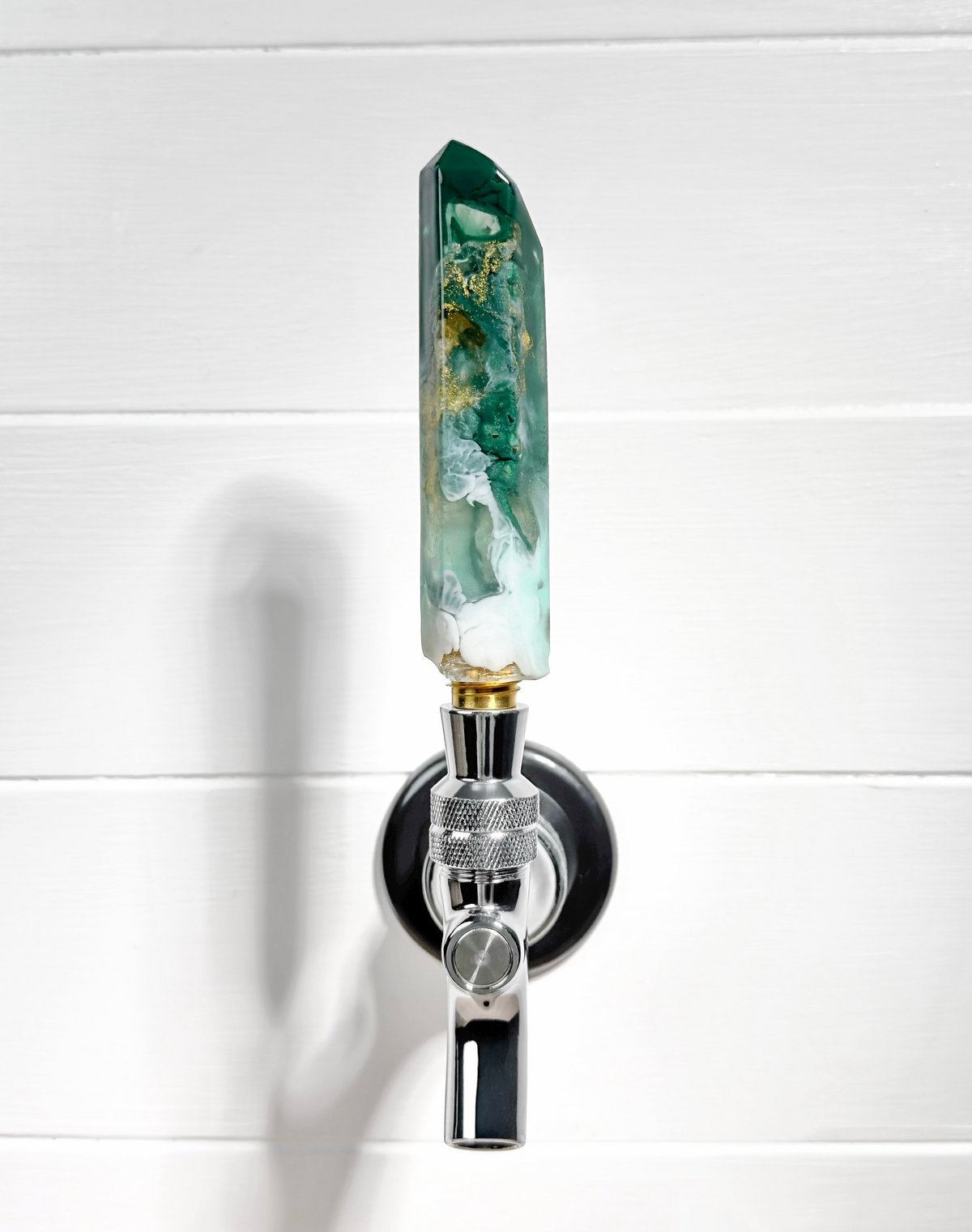 Decorative wall sconce with a green crystal on a white wooden background